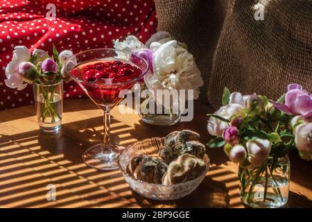 Solenne vita rustica con bicchiere di bevanda rossa con torte in una ciotola circondata da fiori bianchi su sfondo tessile su tavolo di legno. Stri diagonali Foto Stock