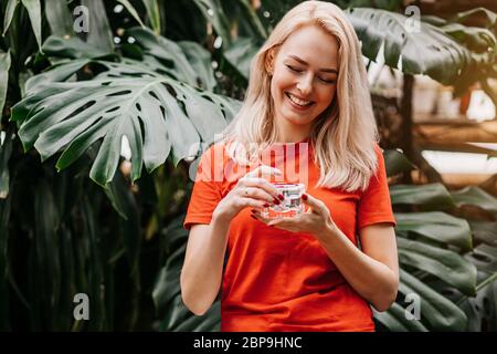 Giovane donna caucasica dall'aspetto buono con pelle sana perfetta che tiene il vaso di crema viso o crema solare, in posa nella foresta pluviale. Cura della pelle, spa, cosmetici, b Foto Stock