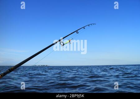 Asta con manovella esca per la cattura di pesci predatori a bordo di una barca contro il blu del mare e del cielo Foto Stock