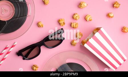 Guardare film con popcorn concetto. Composizione piatta con bicchieri 3d, pop corn in scatola di cartone rosso e bianco, bobine di film e cannucce da bere Foto Stock