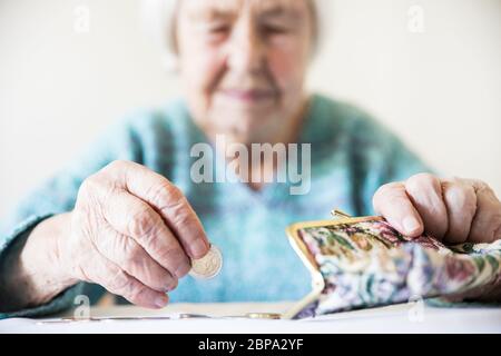 Anziani 96 anni donna seduta miseramente al tavolo a casa e il conteggio delle monete rimanenti dai regimi pensionistici nel suo portafoglio dopo il pagamento di fatture. Unsustai Foto Stock