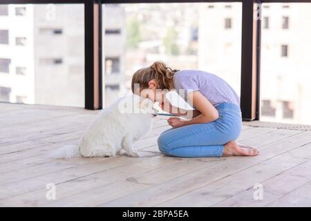 Ragazza adolescente carina che allenano il suo cane spitz a casa. Miglior amico durante la quarantena coronavirus Foto Stock