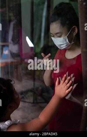 Madre indossare maschera viso incontro figlia e toccare la mano attraverso la finestra a causa della quarantena Corona Virus Covid-19, sociale di distanza Foto Stock