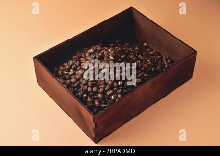 chicchi di caffè naturali in una scatola di legno su sfondo arancione, retroilluminazione morbida e ravvicinata Foto Stock