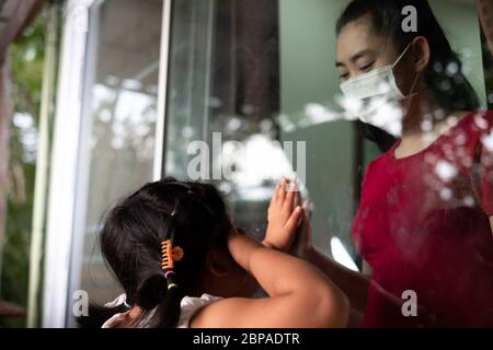 Madre indossare maschera viso incontro figlia e toccare la mano attraverso la finestra a causa della quarantena Corona Virus Covid-19, sociale di distanza Foto Stock