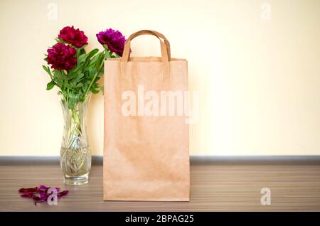 Borsa di carta artigianale per il take away e la consegna di cibo su sfondo giallo. Peony in vaso Foto Stock