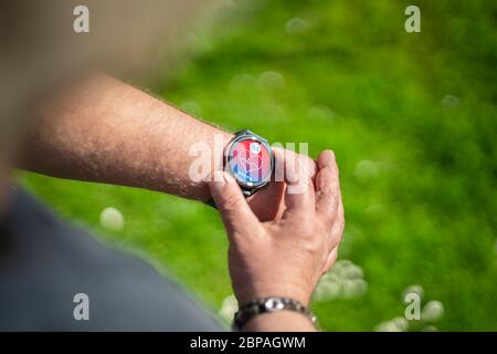 La mano di un uomo chubby indossa un orologio fitness. Vede il suo battito cardiaco. L'app è fittizia e fatta in casa. Foto Stock