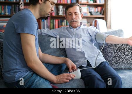 Il giovane misura la pressione sanguigna del padre a casa. Foto Stock