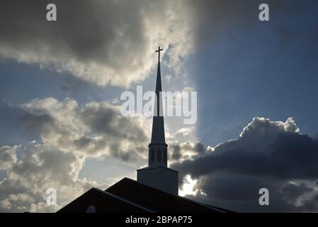 Chiesa Steeple retroilluminato con raggi dal sole tramontare circondato da magnifiche nuvole. Foto Stock