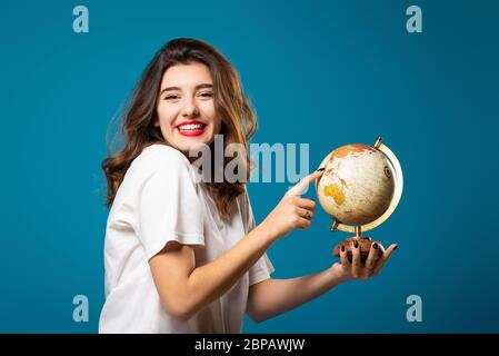 La ragazza sorride e punta a un globo. Isolato su sfondo blu. Concetto di viaggio e turismo Foto Stock