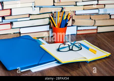 Apri libro di testo, taccuino, occhiali, matite nel contenitore, cartella di plastica, pila di libro. Home distanza formazione concetto di fondo, molti mucchi di libri con Foto Stock