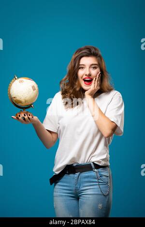 La ragazza sorride e punta a un globo. Isolato su sfondo blu. Concetto di viaggio e turismo Foto Stock