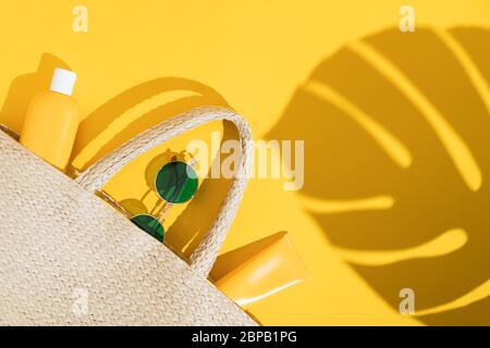 Estate luminoso flatlay su sfondo colorato con sacco di paglia in vimini, tubi o bottiglia con crema solare, occhiali da sole e l'ombra da foglia di monstera. Duro Foto Stock