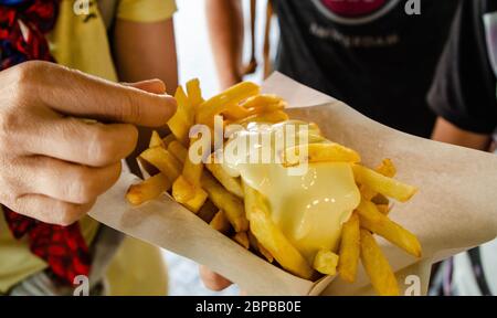 Anversa, Fiandre, Belgio. Agosto 2019. Specialità belga: Patatine fritte guarnite con salsa. La mano immerge un chip di patate nella salsa prima di eatin Foto Stock