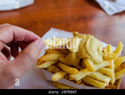 Anversa, Fiandre, Belgio. Agosto 2019. Specialità belga: Patatine fritte guarnite con salsa. La mano immerge un chip di patate nella salsa prima di eatin Foto Stock