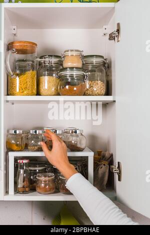 Donna mano apre mensola cucina con vari cereali e semi in vasi di vetro sulle mensole della cucina Foto Stock