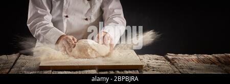 Congelare il movimento esplosione di farina di cottura come chef o cuoco lavora su un cumulo di pasta cruda in una tabella di vintage in un panorama rustico banner con copia spac Foto Stock