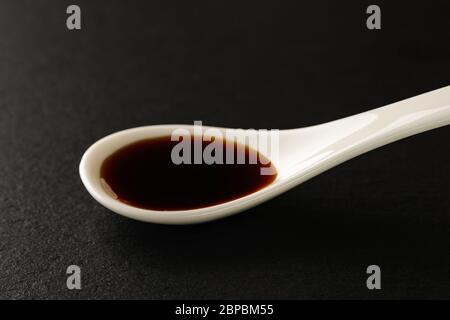 Salsa di soia classica in un cucchiaio di porcellana cinese bianca su un asse di servizio in pietra nera. Salse e condimenti per carne, pesce e verdure. Vista frontale. Foto Stock