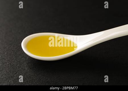 Olio d'oliva in un cucchiaio di porcellana bianca cinese su un asse da servizio in pietra nera. Salse e condimenti per carne, pesce e verdure. Vista frontale. Foto Stock