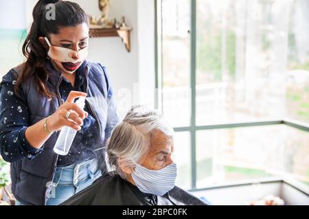 Donna anziana che ottiene un taglio di capelli a casa durante la pandemia Covid-19 indossare maschera facciale Foto Stock