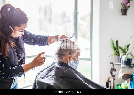 Donna anziana che ottiene un taglio di capelli a casa durante la pandemia Covid-19 indossare maschera facciale Foto Stock