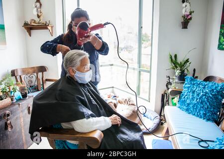 Donna anziana che ottiene un taglio di capelli a casa durante la pandemia Covid-19 indossare maschera facciale Foto Stock