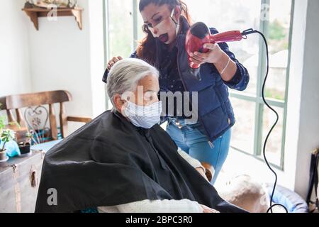 Donna anziana che ottiene un taglio di capelli a casa durante la pandemia Covid-19 indossare maschera facciale Foto Stock