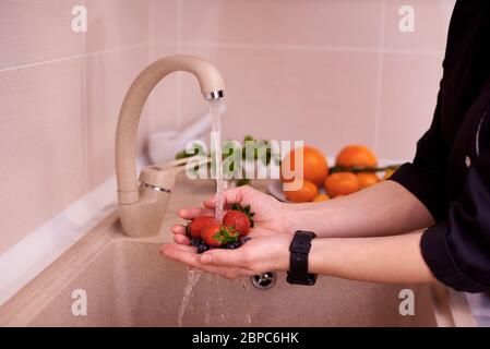 Le mani femminili lavano fragole e mirtilli sotto un flusso d'acqua in un lavandino sulla cucina.fuoco selettivo. Foto Stock