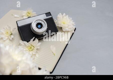 Vecchia fotocamera retrò con bel bouquet di fiori bianchi e blocco note vuoto su sfondo neutro. Blogger o sfondo fotografo Foto Stock