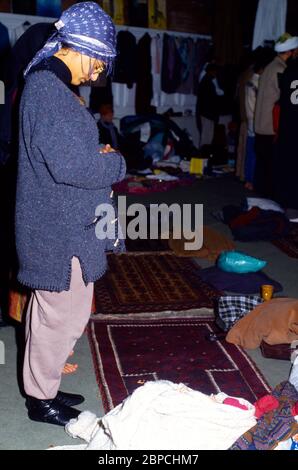 Madre che prega in Moschea con i Bundle del bambino in su sul Rug di preghiera Inghilterra Foto Stock