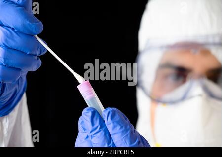Medico tecnico sanitario che tiene COVID-19 kit di raccolta tampone, indossando guanti di protezione DPI bianchi maschera, provetta per il prelievo di campione di campione paziente . Foto Stock