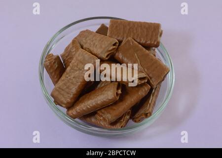 Biscotti crespati al cialda di wafer ricoperti di cioccolato in un recipiente di vetro su sfondo lavanda Foto Stock