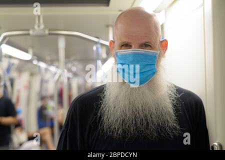 Faccia di uomo calvo maturo con maschera in piedi con distanza all'interno del treno Foto Stock