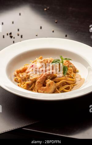 fetuccini di pasta con salsa di gamberi e spezie su un tavolo di legno a piastra bianca Foto Stock