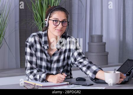 vista di una giovane donna che lavora a casa prendere appunti e utilizzare il computer portatile bere caffè Foto Stock