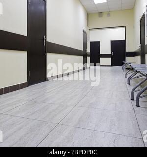 corridoio vuoto nel moderno edificio degli uffici. Ci sono molte porte marroni lungo un corridoio molto lungo con pareti beige. Foto Stock