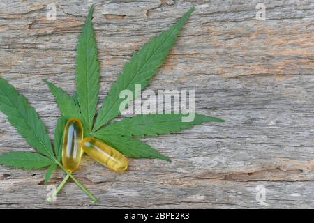 Marijuana medica, capsula di olio di canapa CBD e foglie di cannabis su sfondo di legno. Concetto medico che ricerca foglie di canapa e olio di canapa usando olio come Foto Stock