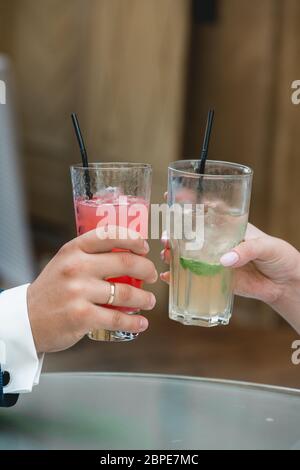 stupendi bride e broom tostando con cocktail alcolici, giorno di nozze. mani che tengono bicchieri Foto Stock