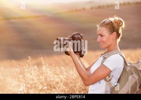 Felice fotografo godere la natura in autunno e sorridente ragazza di viaggiatori con la fotocamera in mano a fotografare golden dry campo di grano in raggi solari Foto Stock