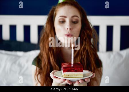 Donna Redhead che soffia una candela di compleanno sulla torta Foto Stock