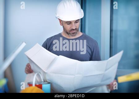 Ritratto di un architetto costruttore che studia la pianta delle stanze, serio ingegnere civile che lavora con documenti sul cantiere, costruzione e h Foto Stock