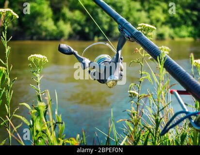 Sulle rive del bellissimo fiume sopra l'alimentatore d'acqua installato - inglese attrezzatura da pesca per la cattura di pesce comodo con la canna e la bobina. Foto Stock