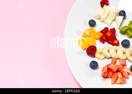 Macedonia di frutta fresca su piatto bianco. Frutta mista in piatto bianco stile alimentare sano. Utile insalata di frutta fresca e frutti di bosco su sfondo rosa Foto Stock