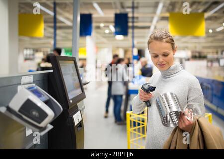 Bella, giovane donna che usa il checkout self-service in un negozio (DOF poco profondo; immagine a colori) Foto Stock