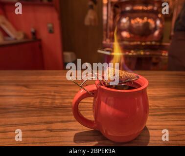 Close-up immagine con un bicchiere di vin brulé, sulla sommità del quale si erge un cono che brucia di zucchero di canna, precedentemente immerso in un sacco di rum. Questa è una tradizione Foto Stock