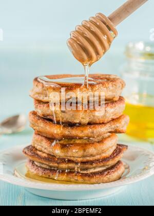 Pila di piccole pancake con banana e semi di chia nel miele su fondo azzurro. Il miele di versarla sulla pila di mini pancake con chia o di papavero, vedere Foto Stock