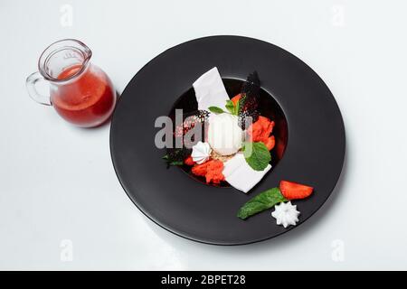 palle di gelato con fragole e sciroppo, decorate con foglie di menta in una ciotola nera su sfondo bianco Foto Stock