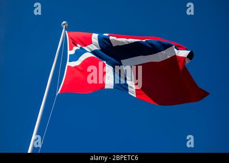 Bandiera della Norvegia in pole sbattimenti nel vento contro il cielo blu e chiaro. Foto Stock