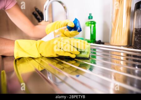 Close-up di persona la mano indossando guanti gialli pulizia lavello in acciaio inox con spugna Foto Stock