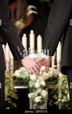 La religione, la morte e il dolor - coppia al funerale holding hands consolante ogni altro in considerazione della perdita Foto Stock